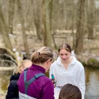 Careerline Tech Students looking at a teacher holding paper, standing outside in cold weather next to a creek